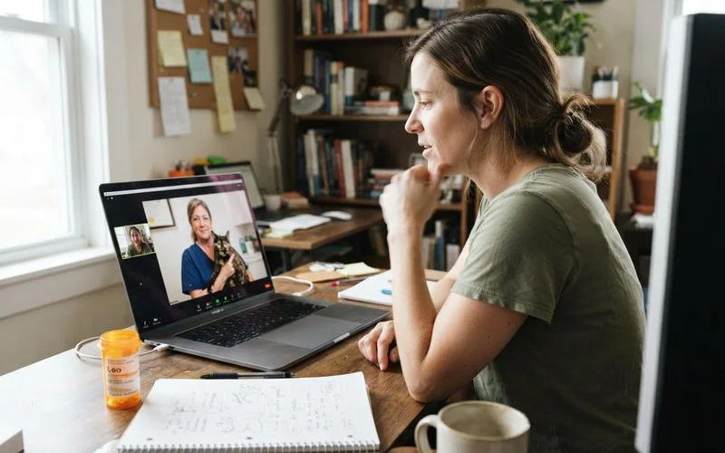 An adult child on a phone call with a veterinary clinic while looking at notes about a parent's pet's medication schedule